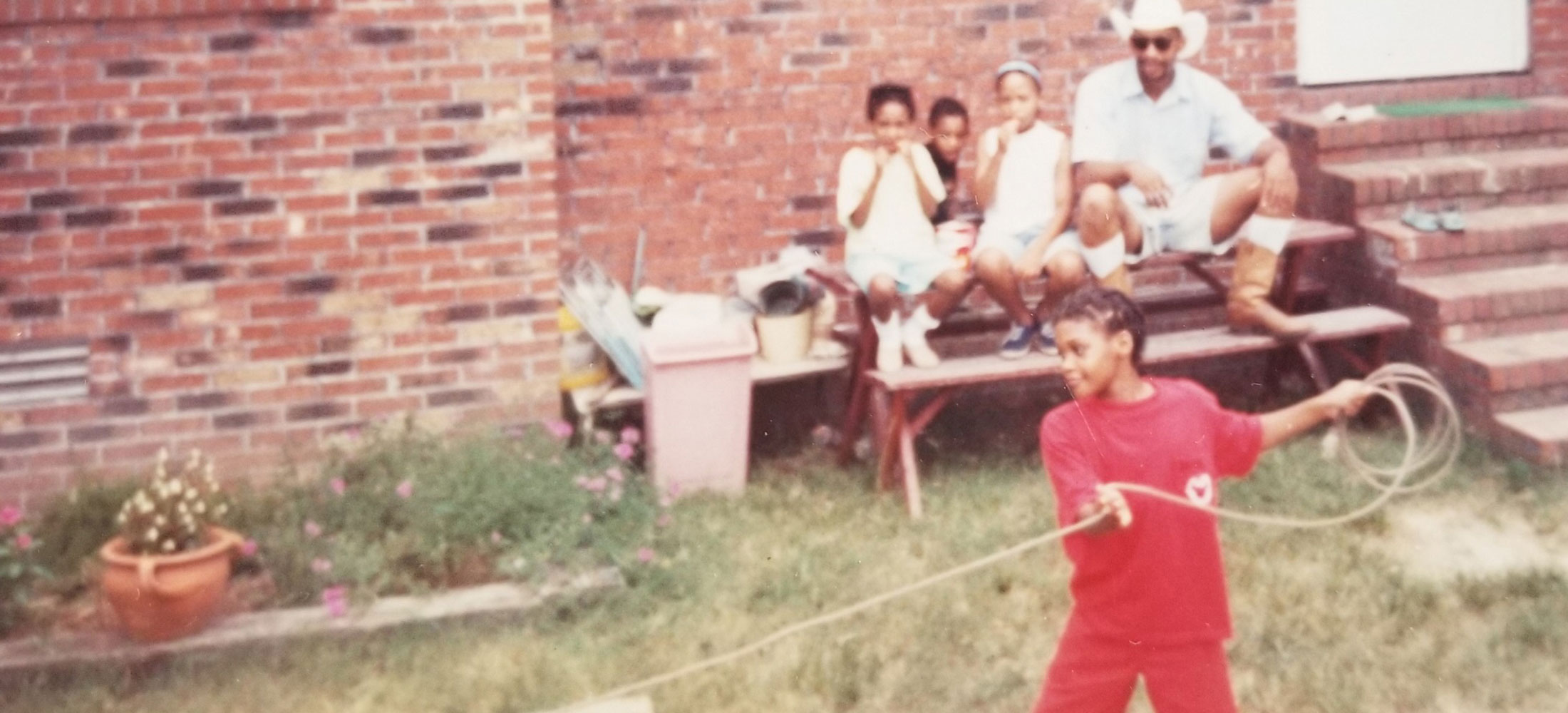 A home photo of a young Candace Dantes roping the dummy and her family sitting watching her.